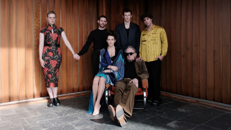 Group of six adults posing formally against a vertical wood-paneled wall on a stone floor.