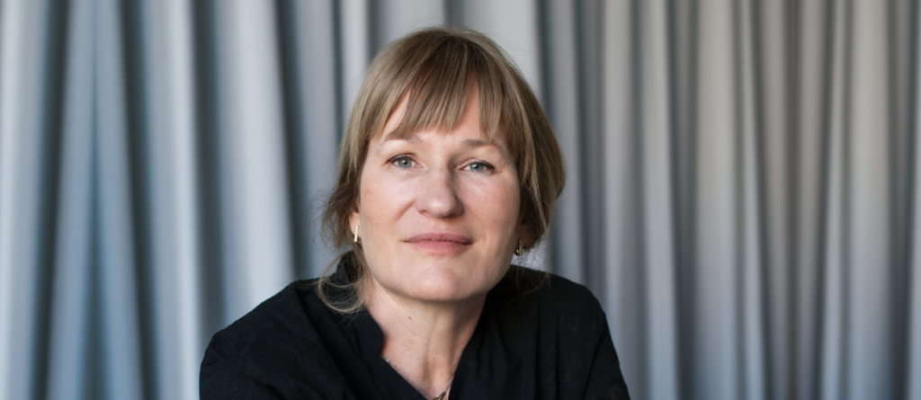 Valeska Grisebach looking forward with a neutral expression against a backdrop of draped grey curtains.
