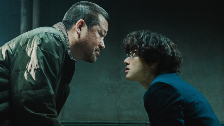 Middle-aged man and a young man with curly hair stare intensely at each other in a dimly lit, blue-toned room.
