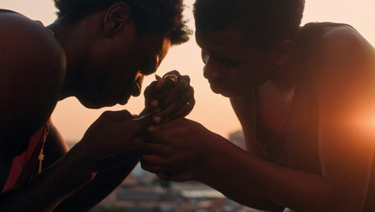 Two people lean inward against a golden sunset, their hands clasped together in a gentle, focused embrace.