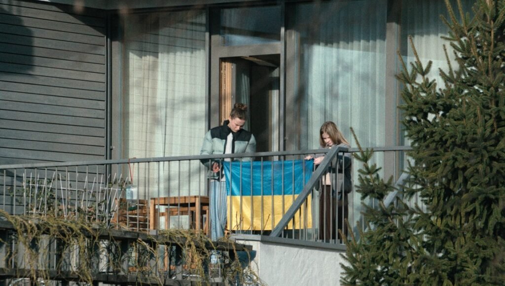 Woman and girl hang a blue and yellow Ukrainian flag over a metal balcony railing.