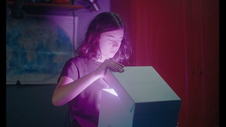 Young girl opening a glowing white box in a dimly lit room with purple ambient lighting.