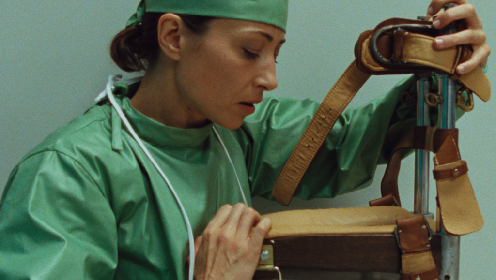 Woman in green surgical scrubs intently examines a leather and metal medical restraint device.