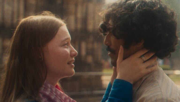Young woman tenderly holding the face of a man with curly hair in a warm, cinematic light.