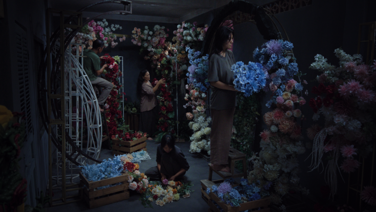 Four people in a dimly lit room arrange large, colorful floral displays on circular metal frames.
