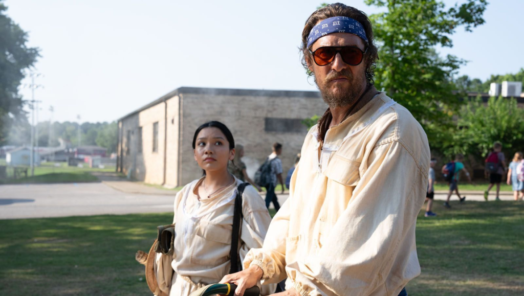 A man wearing a blue bandana and amber sunglasses walks beside a woman outdoors in a sunny field.