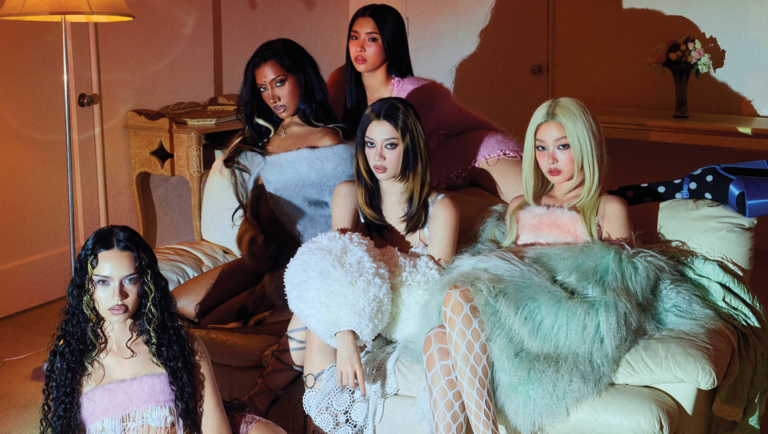 Five members of KATSEYE posing together in a dimly lit room with vintage decor and warm lighting.