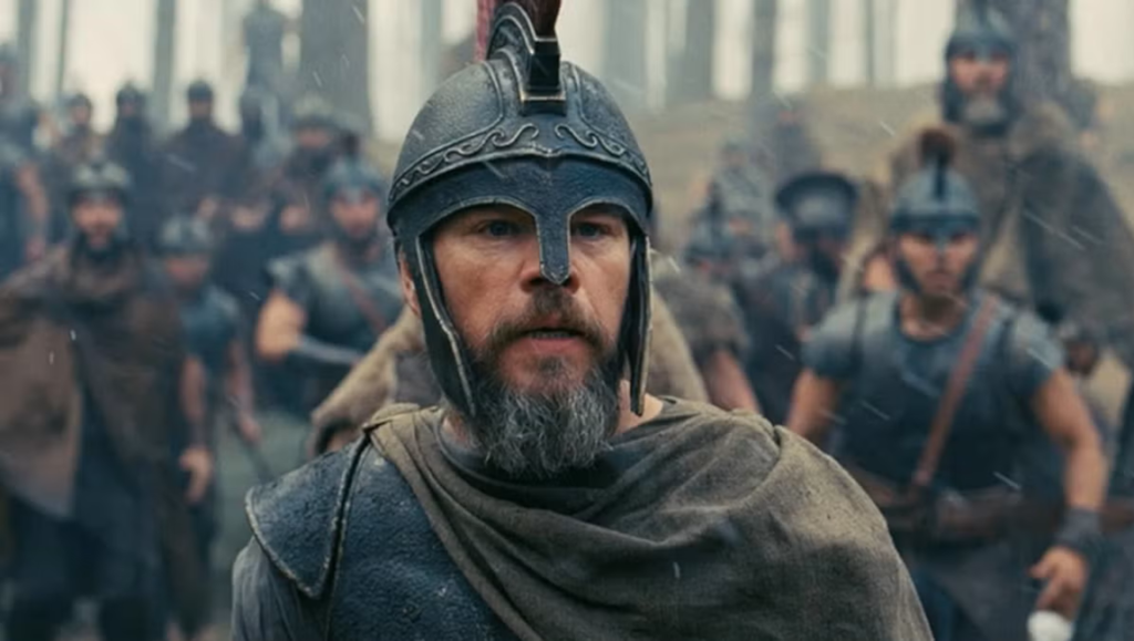 Bearded soldier wearing an ornate metal helmet and cape leads a battalion of infantry through a misty forest.