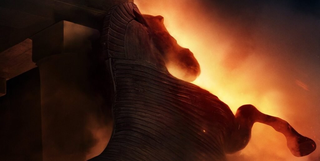 Wooden Trojan horse silhouette stands illuminated against a backdrop of intense, glowing orange flames.