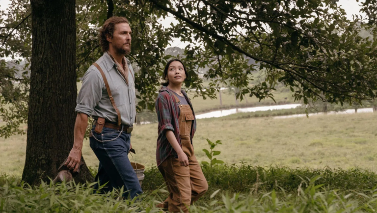 Matthew McConaughey and a young woman walk through a grassy field near trees in The Rivals of Amziah King.