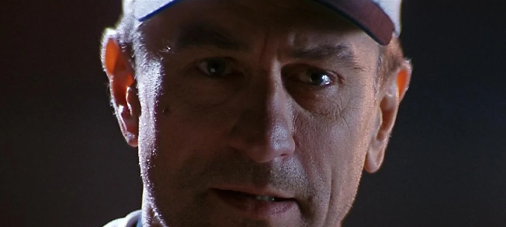 Betrayed By the Game: On Tony Scott, Baseball, and The Fan at 30 Close-up of Robert De Niro wearing a baseball cap with a serious, intense expression in a dimly lit scene.