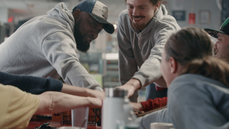 Diverse group of people smiling while stacking their hands together over a table in a brightly lit room.
