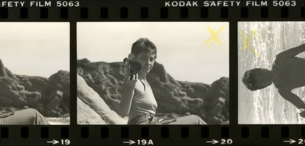 Film strip frames showing a person filming with a vintage camera on a rocky beach and a swimmer in splashing water.