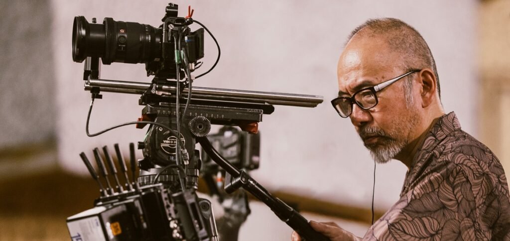 Shinya Tsukamoto with glasses operating a professional film camera on set
