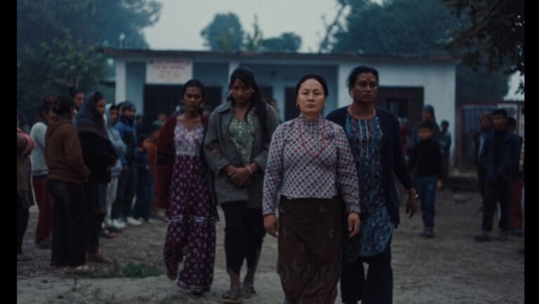 Four women walk side-by-side in a line outdoors in front of a crowd under a cloudy sky.