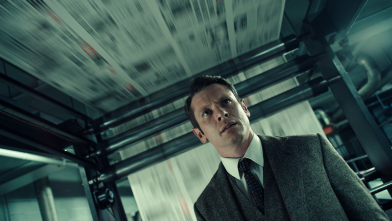 Man in a suit and tie looking upward in an industrial setting with blurred papers flying above.