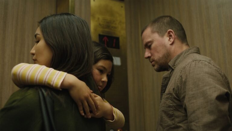 Young girl in a striped shirt hugs a woman inside an elevator while a man stands nearby looking down.