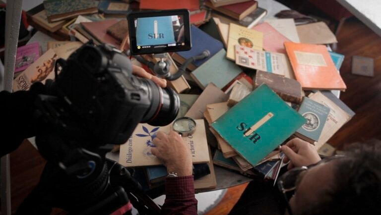Hands examine books with magnifying glass and tweezers as a camera films for SLR.