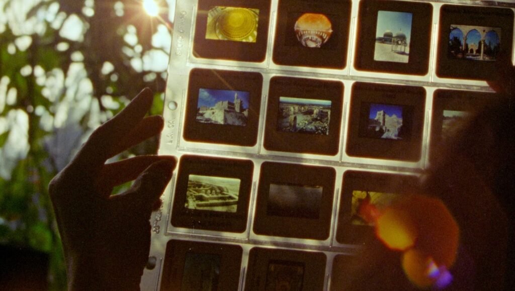 Hand holds a plastic sheet of 35mm film slides against bright sunlight to view architectural photographs.