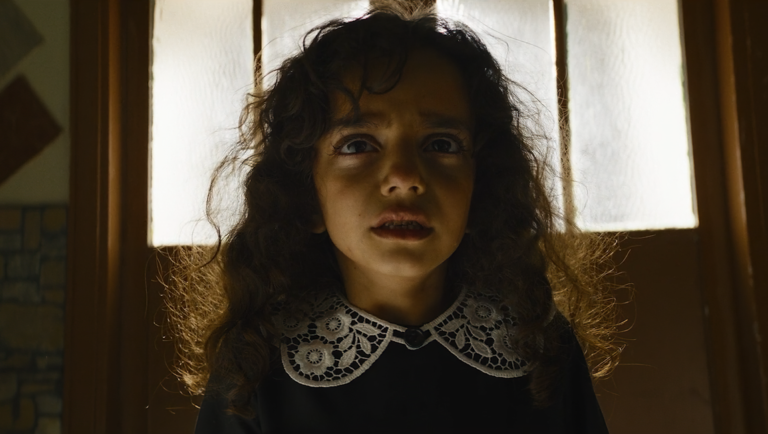 Frightened girl with curly hair and a lace collar stares upward in warm backlight.