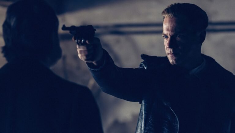 Man in a leather jacket aims a revolver at a silhouetted figure in dim blue light.