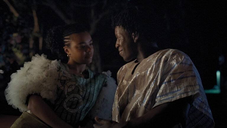Smiling woman in ruffled top and man in patterned robe embrace at night outdoors