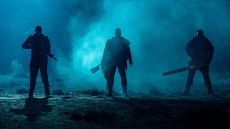 Three menacing figures in dark clothing stand in blue fog, wielding a rifle, a meat cleaver, and a chainsaw.