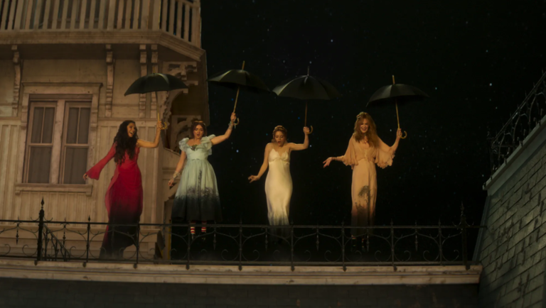 Four women in vintage dresses hold black umbrellas while leaping from a house balcony against a dark, starry night sky.