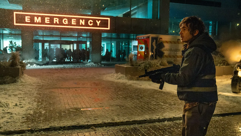 Man holding a rifle stands in snowy street outside hospital emergency entrance at night