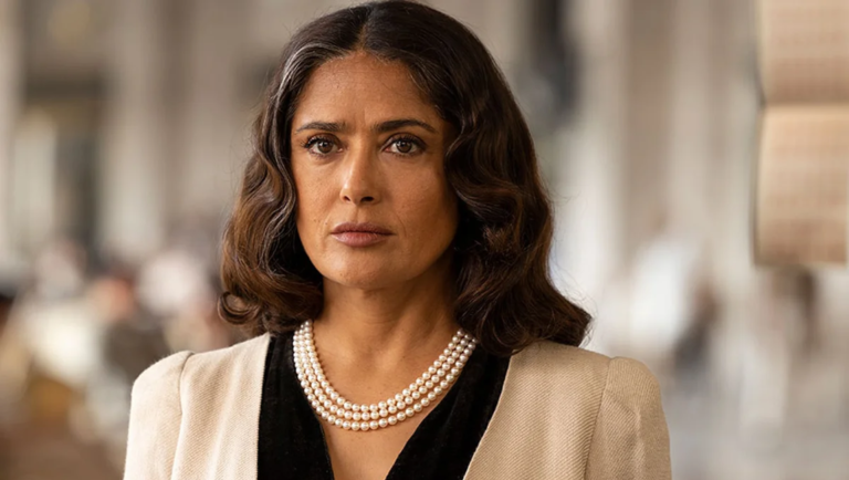 Salma Hayek wearing a triple-strand pearl necklace and beige blazer, looking solemnly at the camera