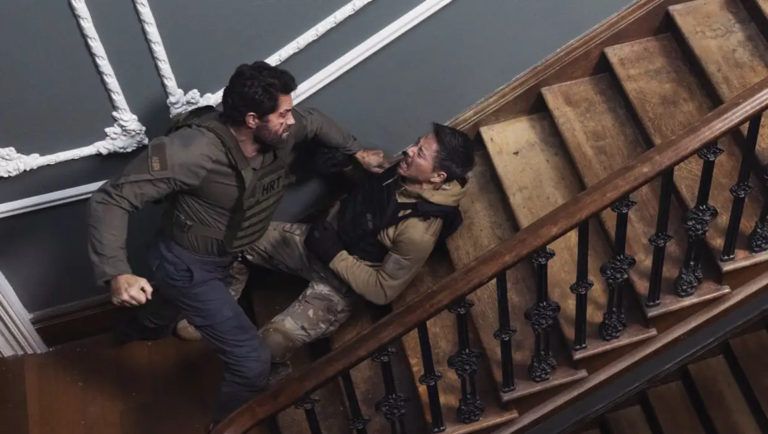 Two men in tactical gear fighting on a wooden staircase with ornate iron railings.