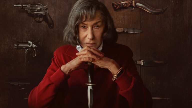 Woman in a red blazer clasps her hands over a dagger, surrounded by mounted firearms and blades on a dark wooden wall