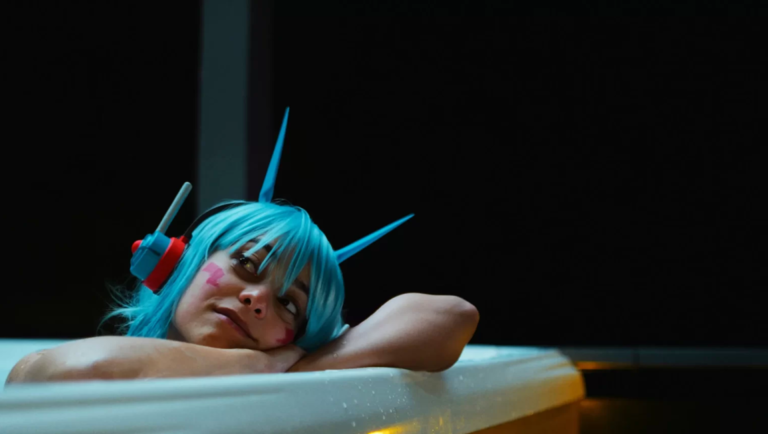 Woman in blue wig and pink face paint resting arms on a white bathtub edge in dark bathroom