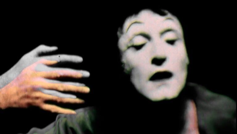 Pale face with closed eyes and open mouth beside a raised hand against black background