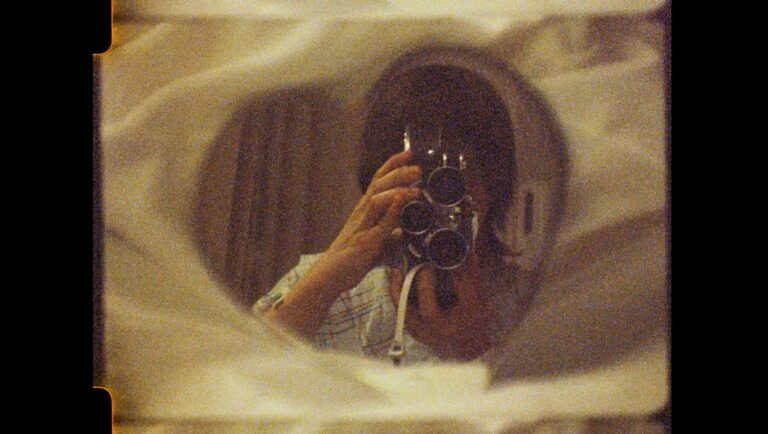 Hands holding a vintage movie camera with three lenses, filming a reflection in a circular mirror
