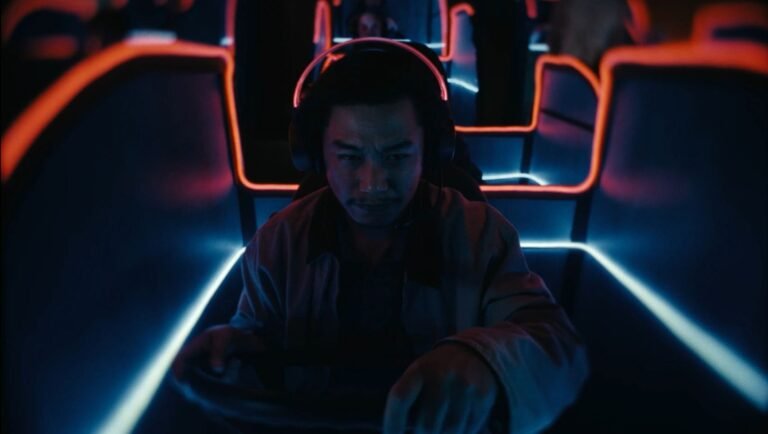 Man in headphones sits in a dim booth lit by neon blue and orange light.