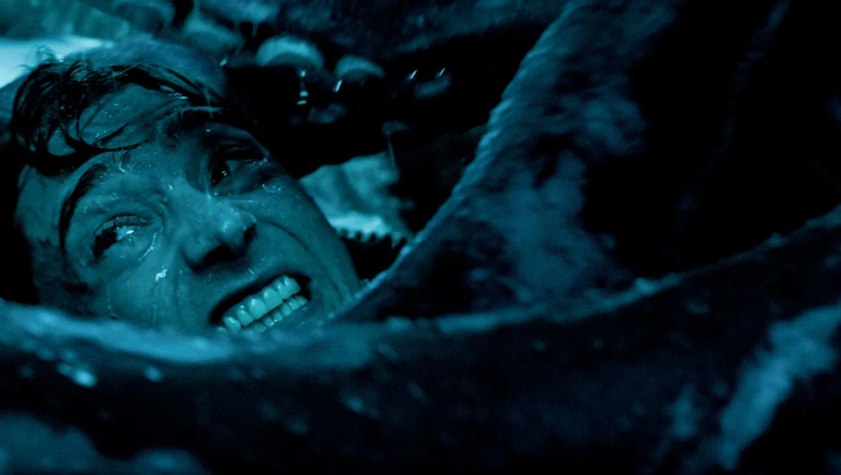 Close-up of a terrified man grimacing with gritted teeth while wedged inside the dark, blue-tinted folds of a giant whale's mouth.
