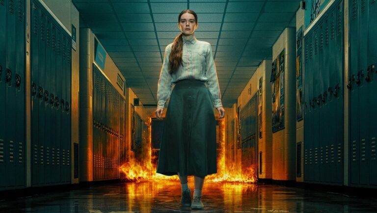Girl in a long skirt and sweater stands in a school hallway as flames rise behind her.
