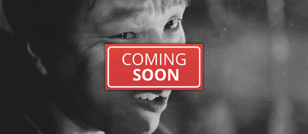 Black-and-white close-up of a smiling person with a red "COMING SOON" banner covering their mouth