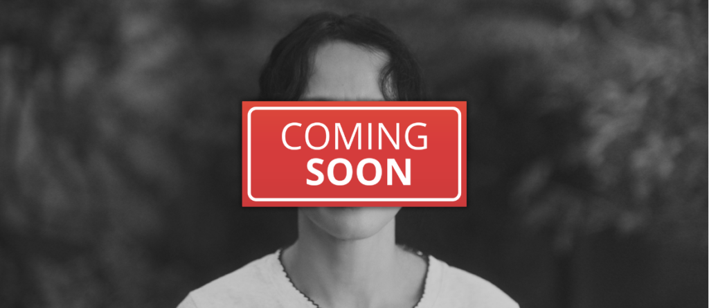 Black-and-white portrait of a person in a light top, face hidden by a red 'COMING SOON' sign, blurred foliage behind