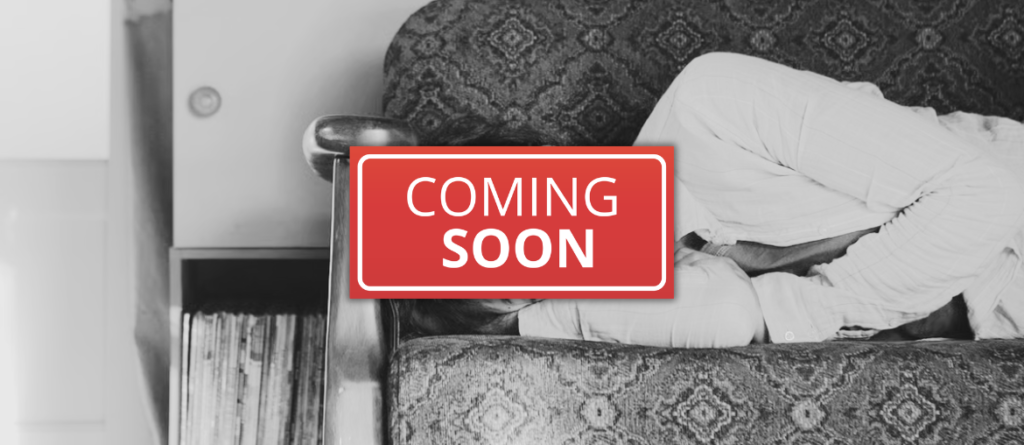 Person curled up on a patterned sofa with a red 'COMING SOON' label across the frame, a shelf of records nearby