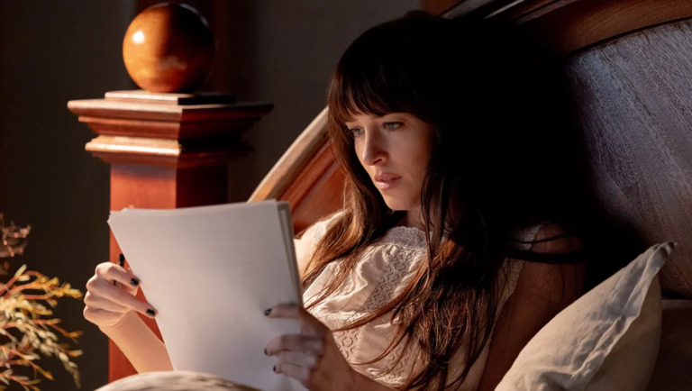 Woman sitting up in bed reading a document by warm lamp light